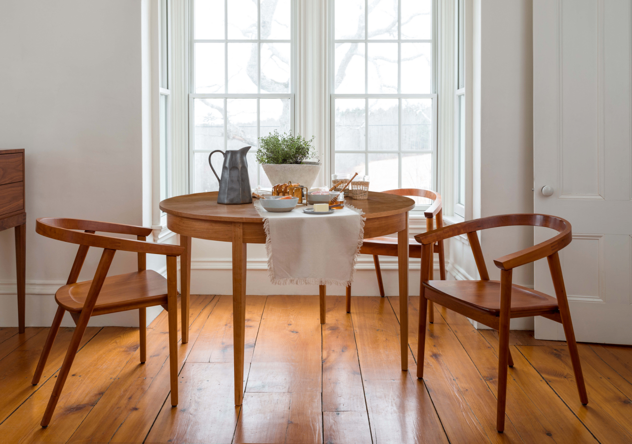 A round ring table and cumberland chairs in cherry sits in a breakfast nook with several food items on the table top.