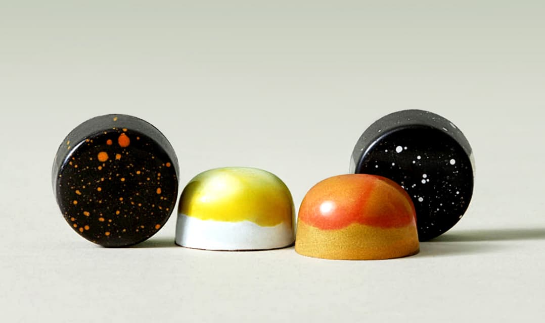 The four varieties of Aperitivo & Digestivo bonbons. Two are dark brown with speckles. The other two are shades of orange and yellow.