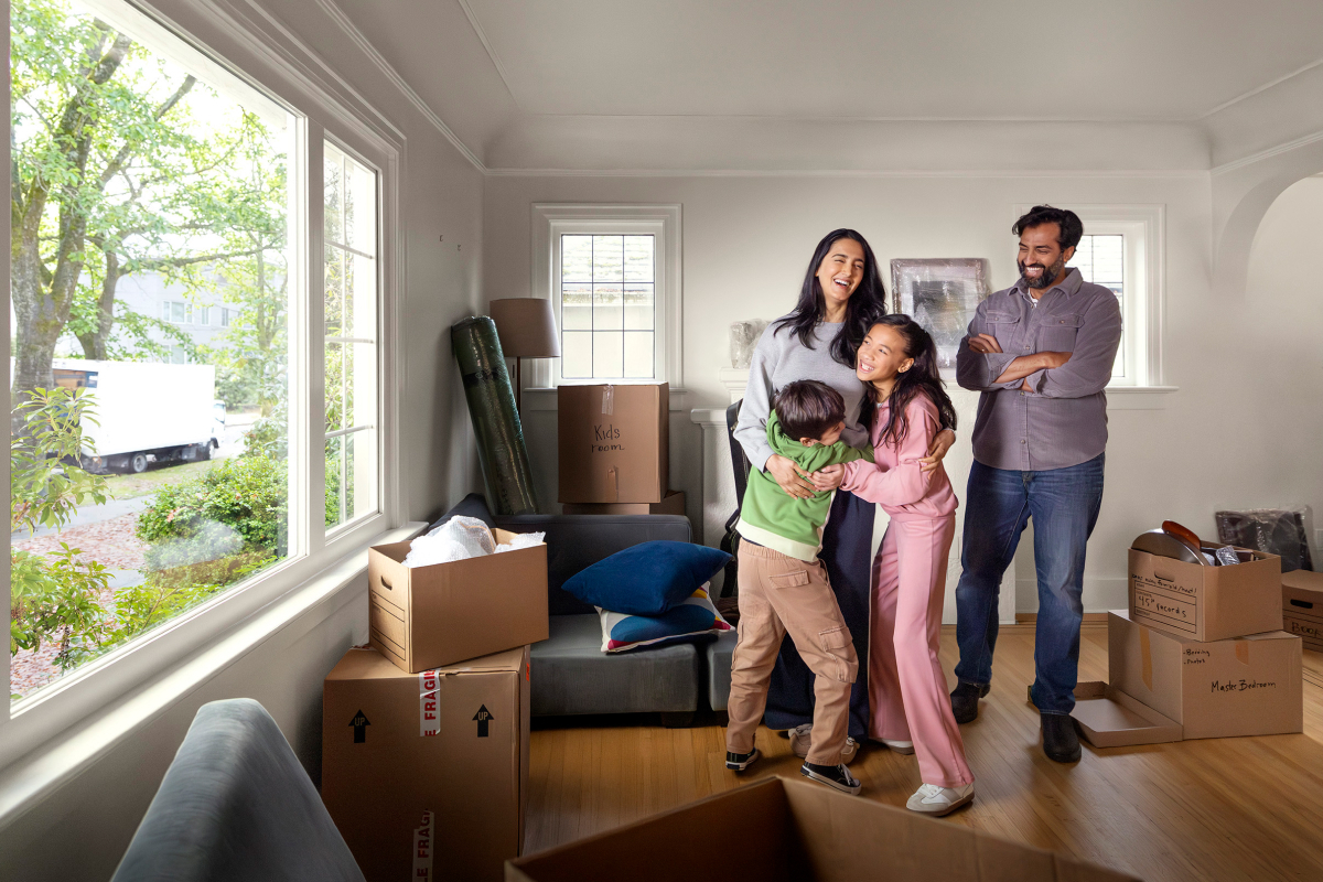 A family stands happily inside their new home surrounded by moving boxes.