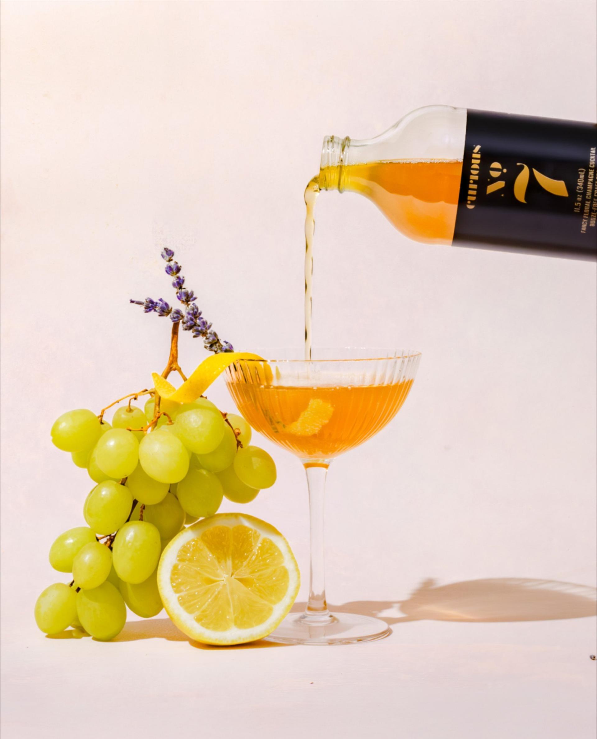 Curious No. 7 bottle being poured into a coupe with a lavender sprig garnish and green grapes sitting on its side.