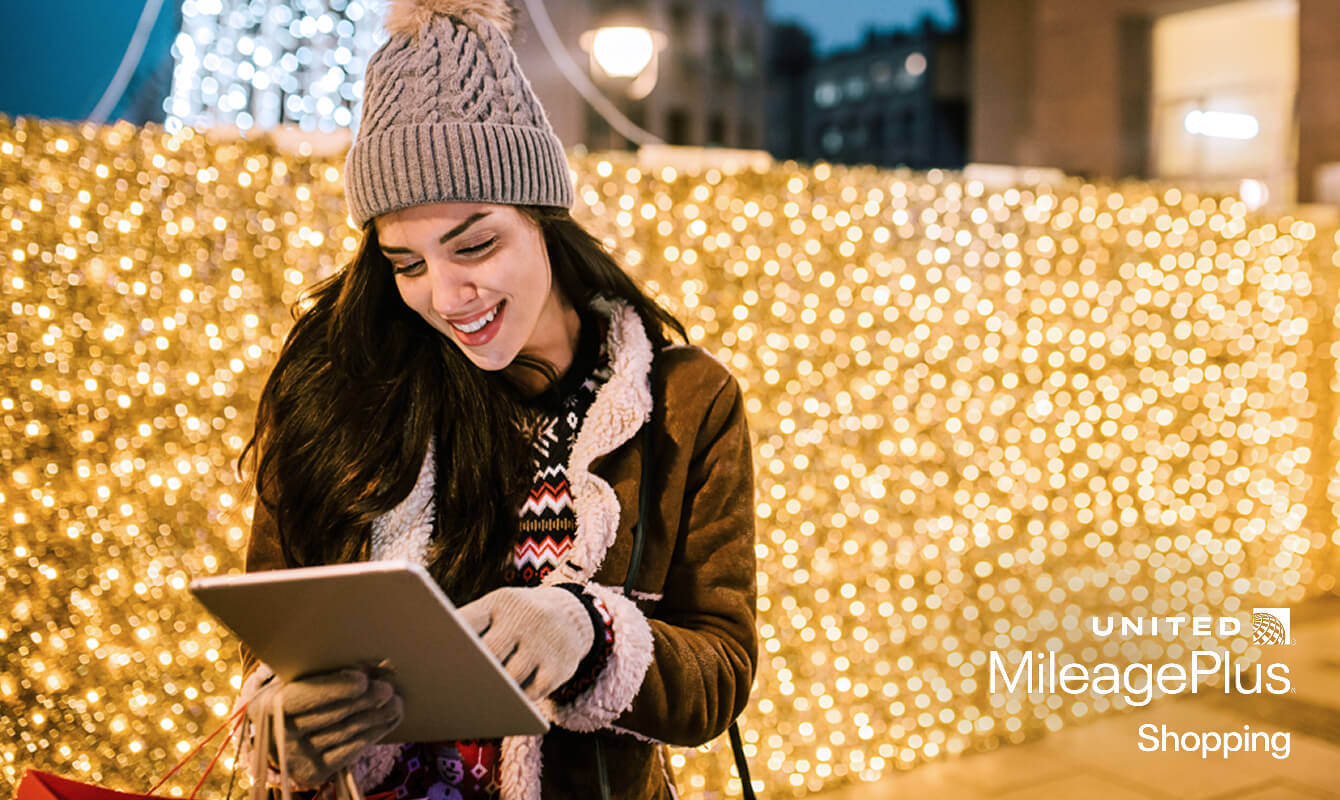 A woman scrolls on her tablet while holiday shopping in a city that's decorated with illuminated trees and decorations
