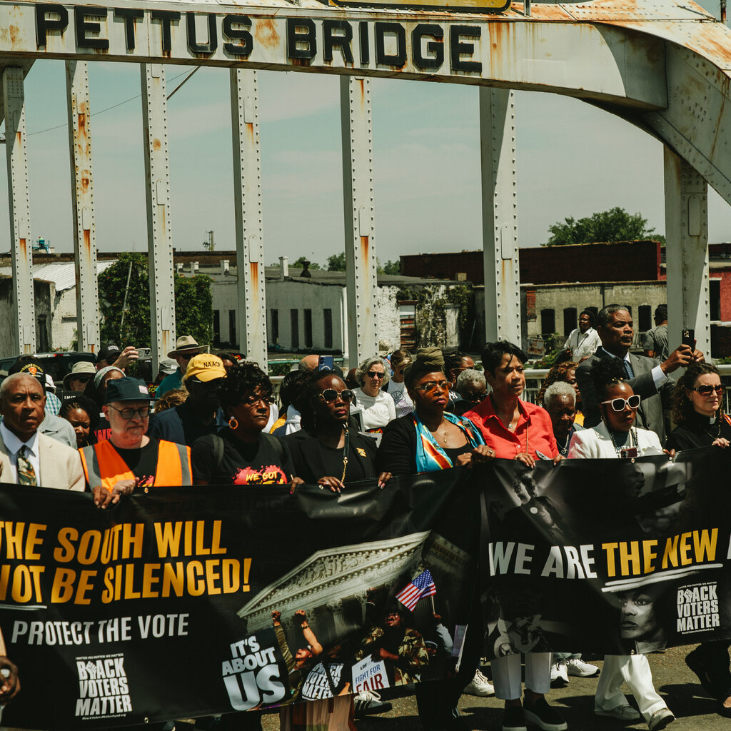People holding banners and walking across the Edmund Pettus Bridge.