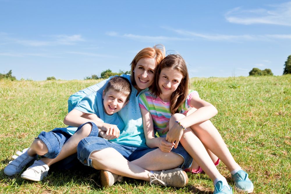 Lisa and her two children sat on grass, cuddled together, smiling.