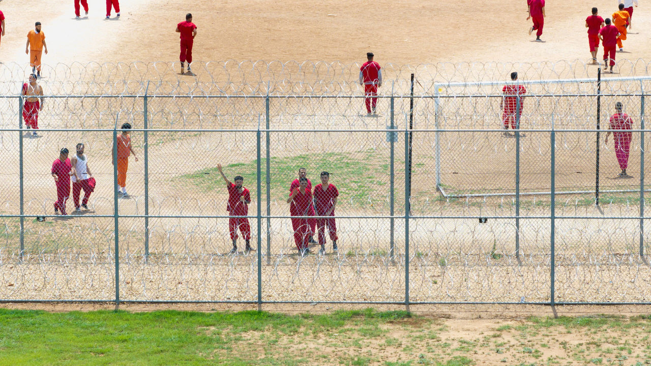 Drone view of detainees looking at a drone from behind the fence while exercising in the courtyard