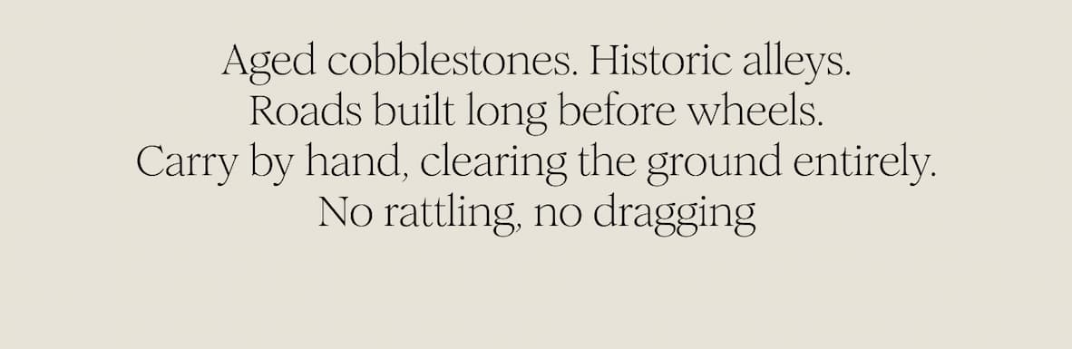 Aged cobblestones. Historic alleys. Roads built long before wheels. Carry by hand, clearing the ground entirely. No rattling, no dragging