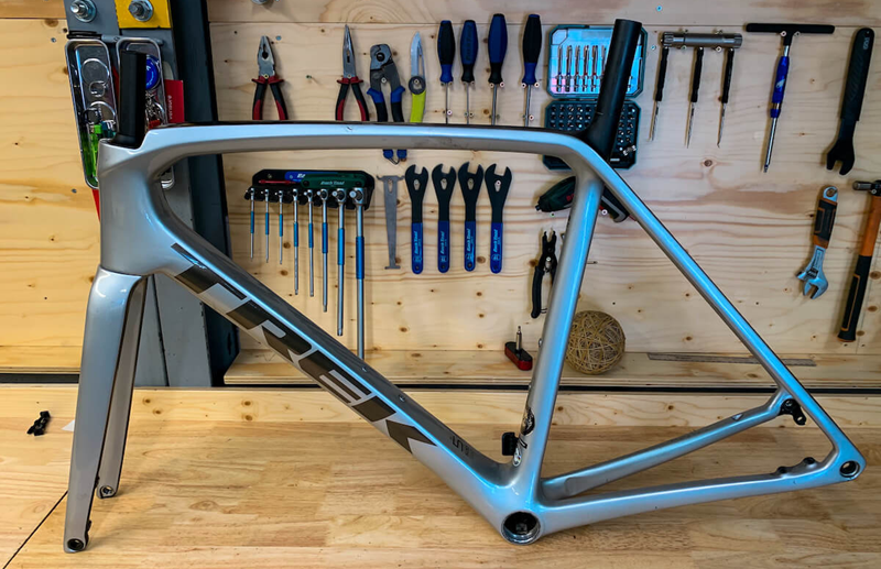 A Trek bike frame propped up on a wooden work bench, with tools hung in the background.