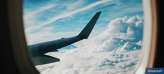 A view out of an airplane window filled with puffy clouds and the plane&rsquo;s wing