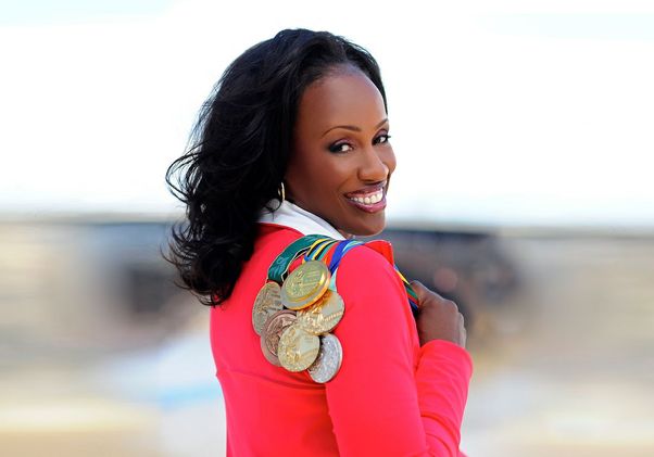 Jackie Joyner-Kersee in red jacket, looking back over her shoulder while holding Olympic medals
