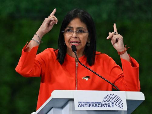 Figure stands at podium making hand gesture