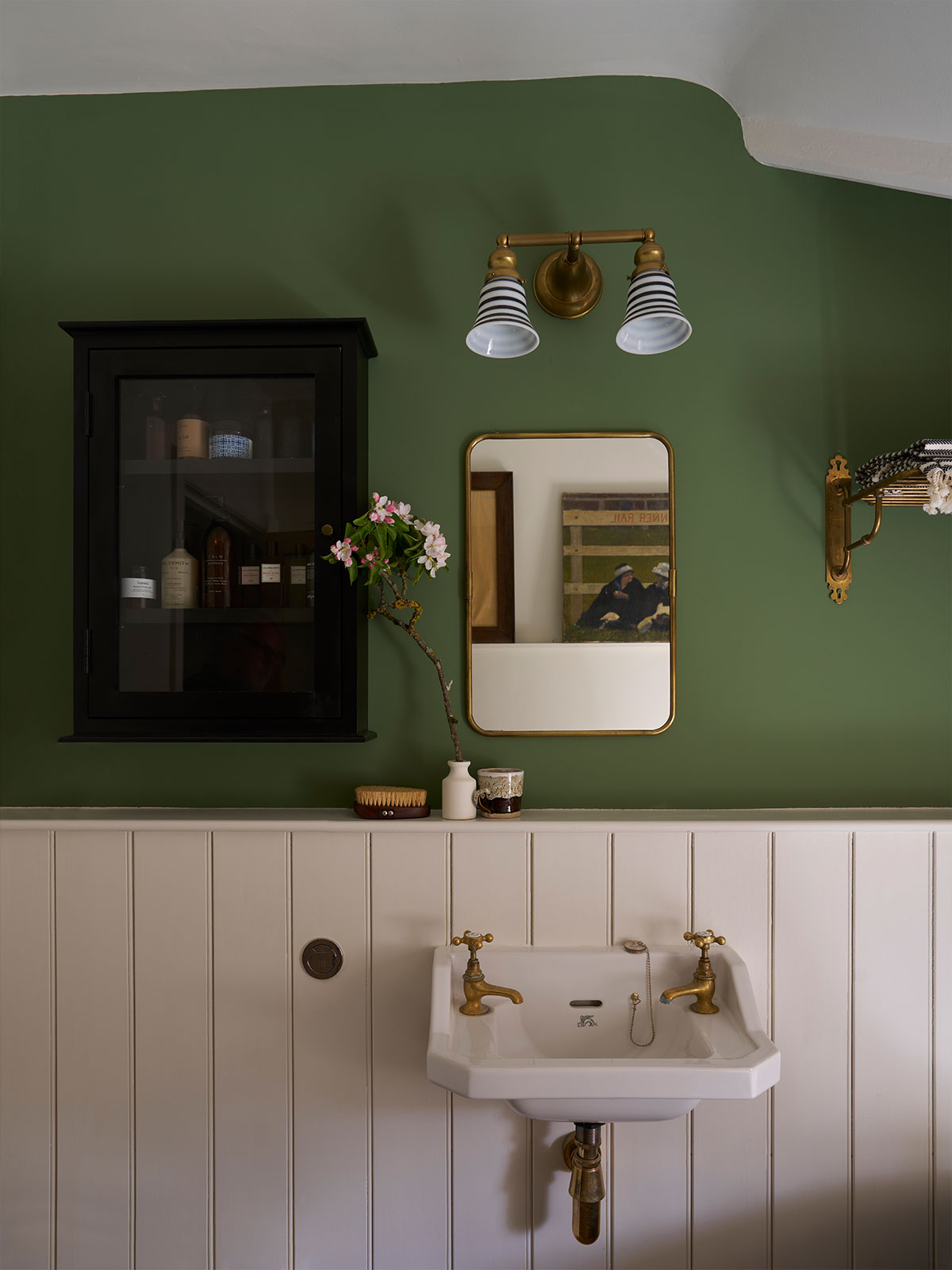 Rich cream wooden panelling contrasts with the intense green wall above it. This might only be a cloakroom space but it’s one with plenty of impact. An antique wooden cabinet provides useful storage for additional jars and bottles, while the mirror reflects light into the space. The whole room is softened with a sprig of blossom in a ceramic vase.