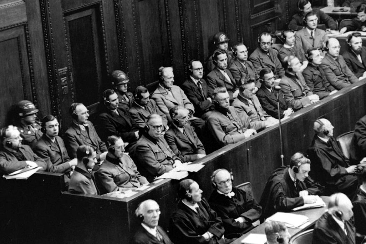 Black-and-white photo of rows of men wearing suits and headphones sitting in a courtroom
