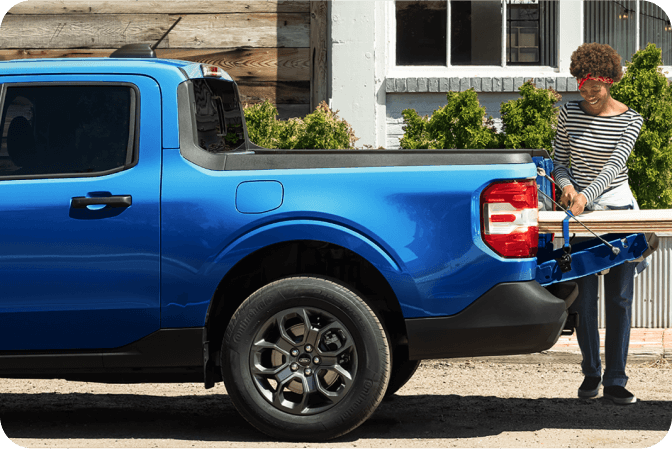 A woman using the Ford Maverick&reg; truck&rsquo;s FLEXBED&reg; Storage System to load planks of wood