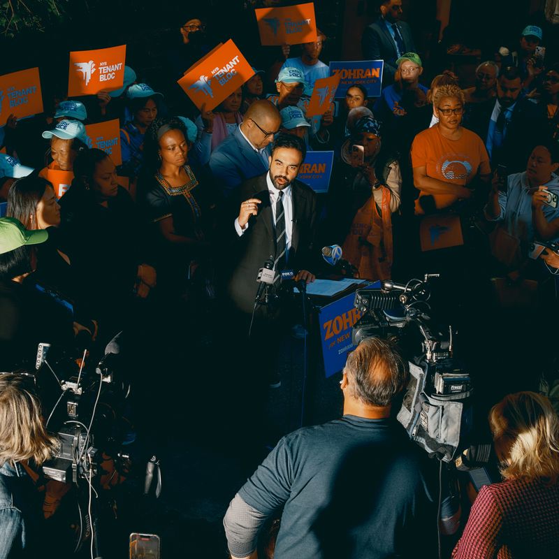 A man in a suit speaks to a crowd of supporters and media.