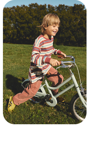 Young boy in striped shirt riding white bike on grass with trees in background