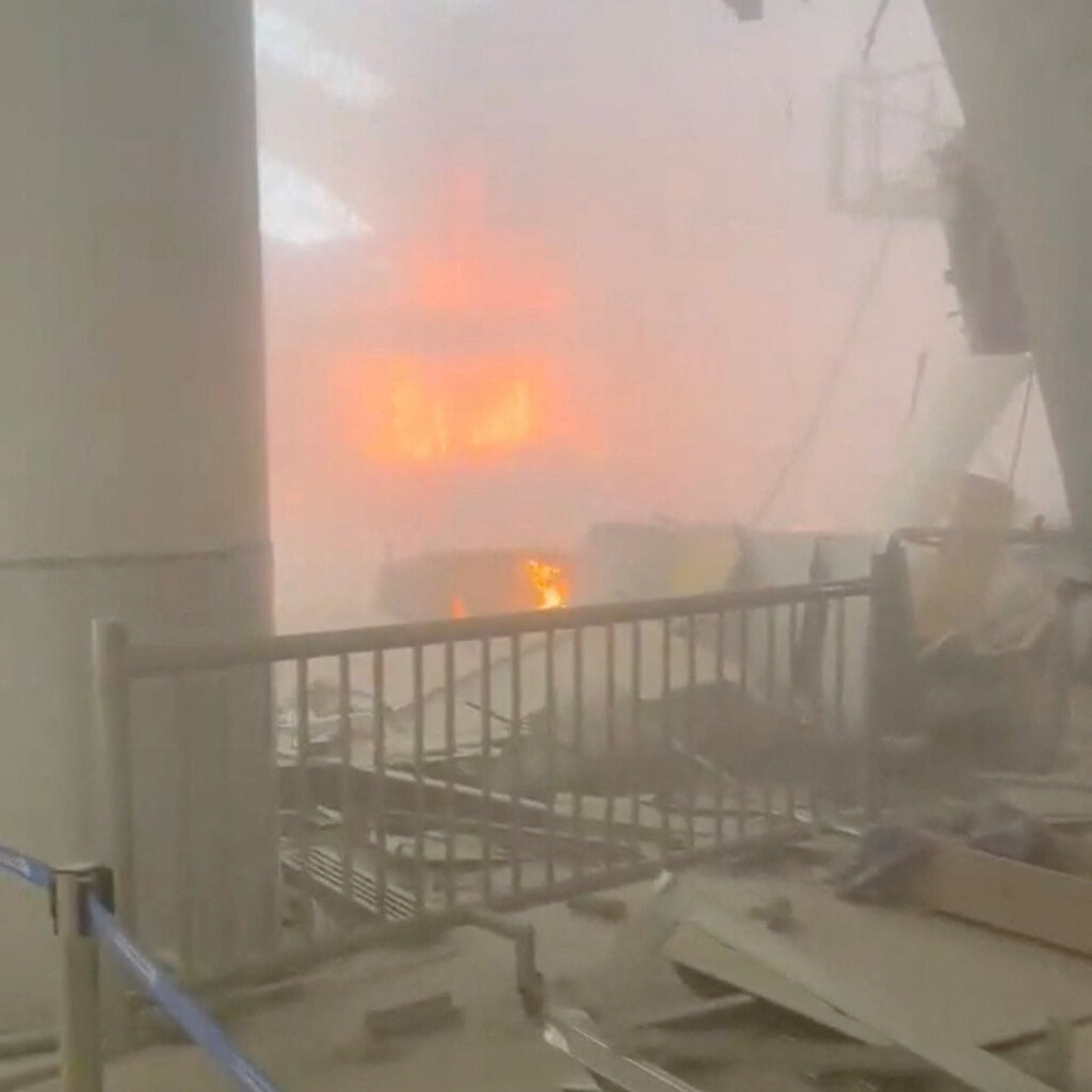 Fire burns in an airport terminal, which is littered with debris and broken panels.