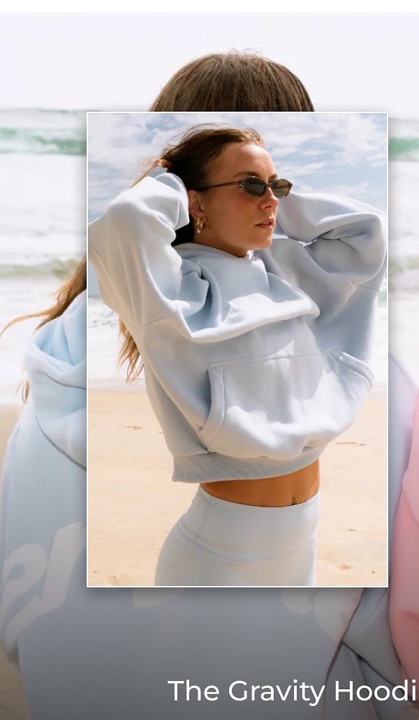 A person wearing a light blue hoodie and sunglasses at the beach.