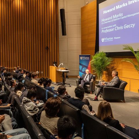 Two speakers engaged in a fireside chat in front of an audience.