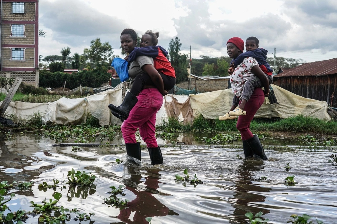 Women carry children on their backs as they wade through a flooded street in Kihoto, a low-income community severely affected by the rising waters of Lake Naivasha. 