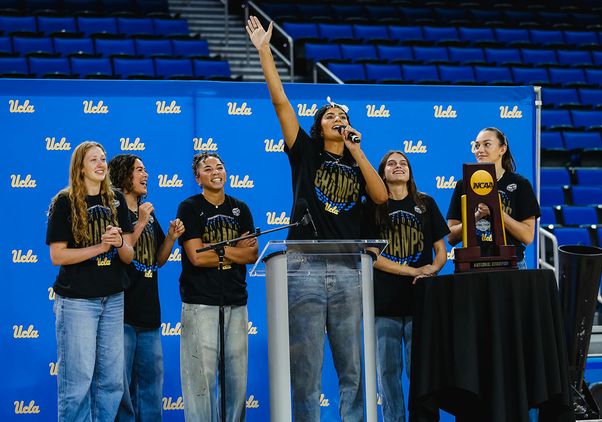 UCLA women's basketball team members stand in front of a UCLA step-and-repeat banner