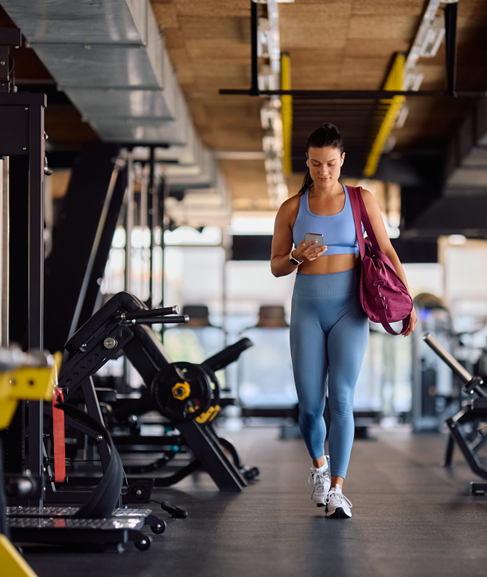 Woman at gym with phone and bag.