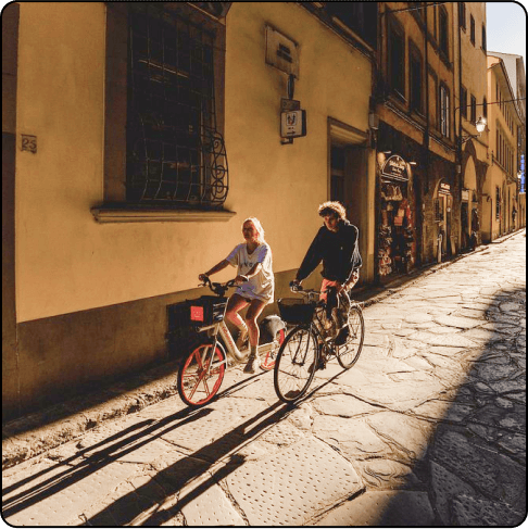 Image Description: A man and a woman on bikes riding through a cobblestoned street at sunset.