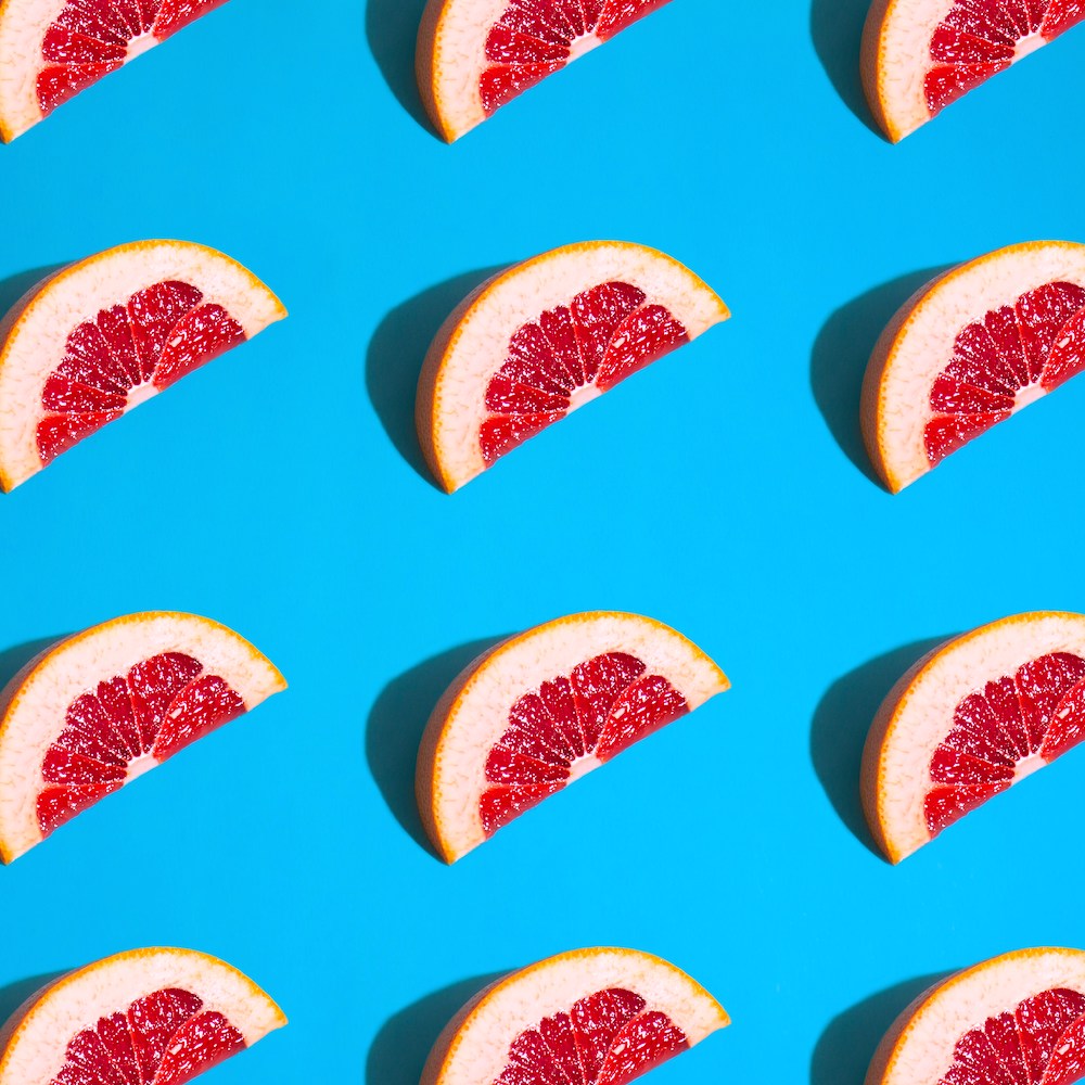 Several slices of blood orange arranged in a pattern on a bright blue background.