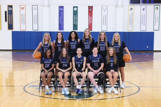 Women's basketball team poses for a group shot, wearing black and blue uniforms.