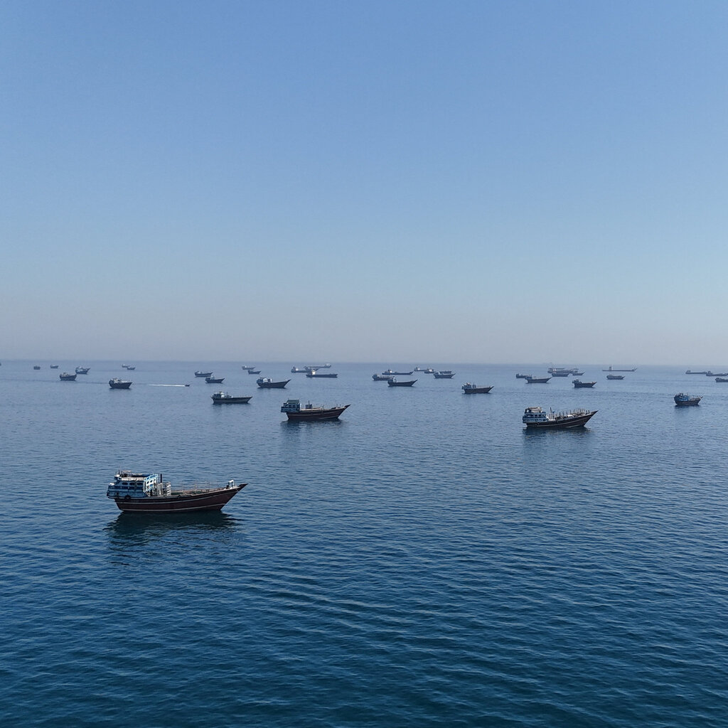 Numerous vessels on calm water under a cloudless sky. The horizon cuts through the center of the photo. 