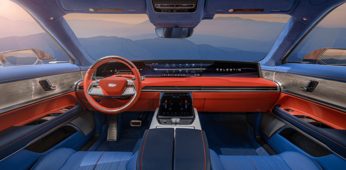 Shot of the luxurious interior of the Cadillac CELESTIQ, showcasing the wide digital display that spans the entire width of the vehicle, the steering wheel, and cabin upholstered in a rich blue fabric with red accents.