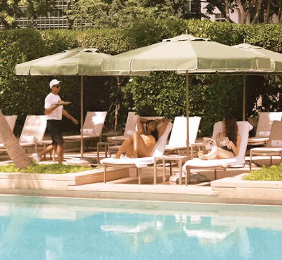 Poolside scene with loungers, green umbrellas, and a staff member serving drinks.