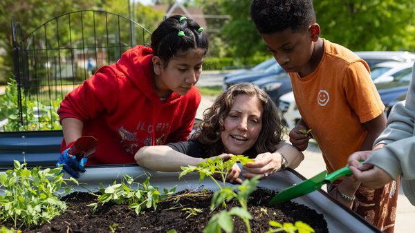 woman and two children look at small plants in a planter bed