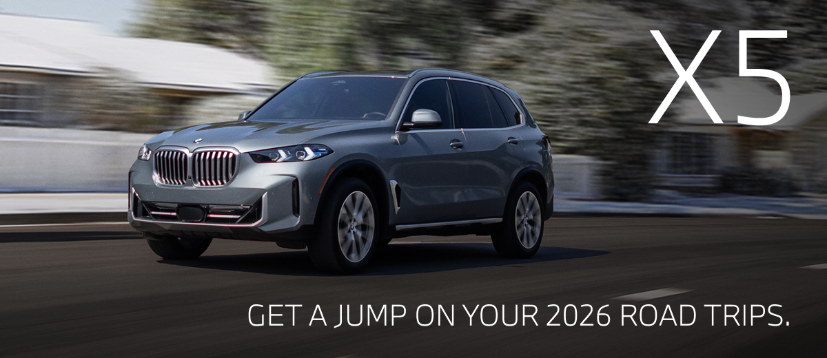 2026 BMW X5 driving down a winter road with snowy trees in the background