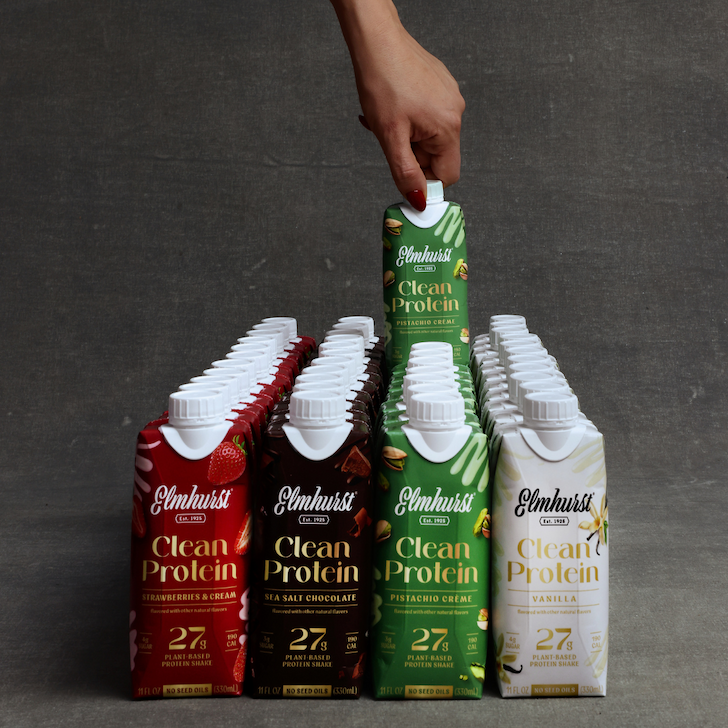 Hand reaches for a Pistachio Crème Elmhurst Clean Protein shake from a large grid of Strawberries & Cream, Sea Salt Chocolate, Pistachio, and Vanilla cartons.