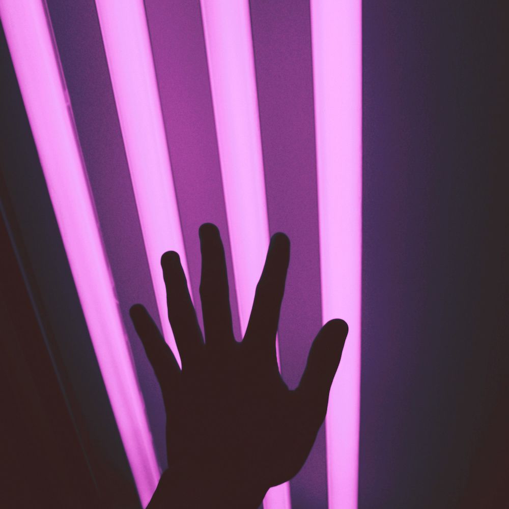 A reaching hand is silhouetted against four bright pink fluorescent lights.