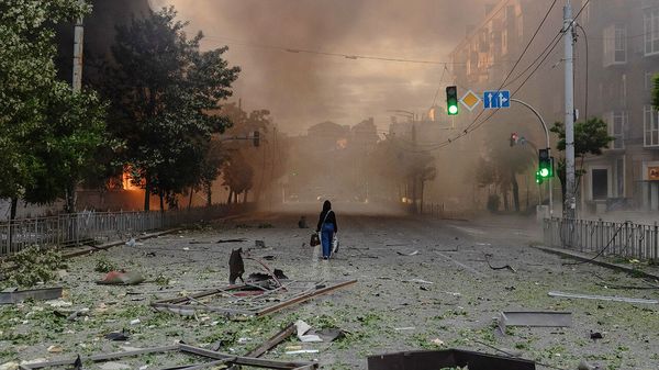 A woman walks along a smoke-filled road beside heavily damaged buildings following Russian strikes in Kyiv.