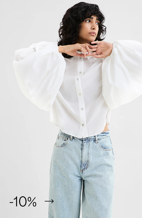 Emma in The Fulton Top, a button-up blouse with oversized puff sleeves, styled with light blue jeans.