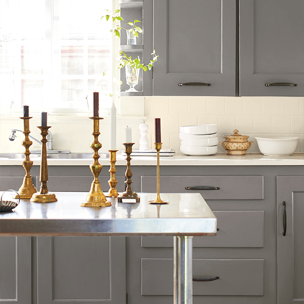 A kitchen with gray painted cabinets, an off-white wall, and a stainless steel worktable.