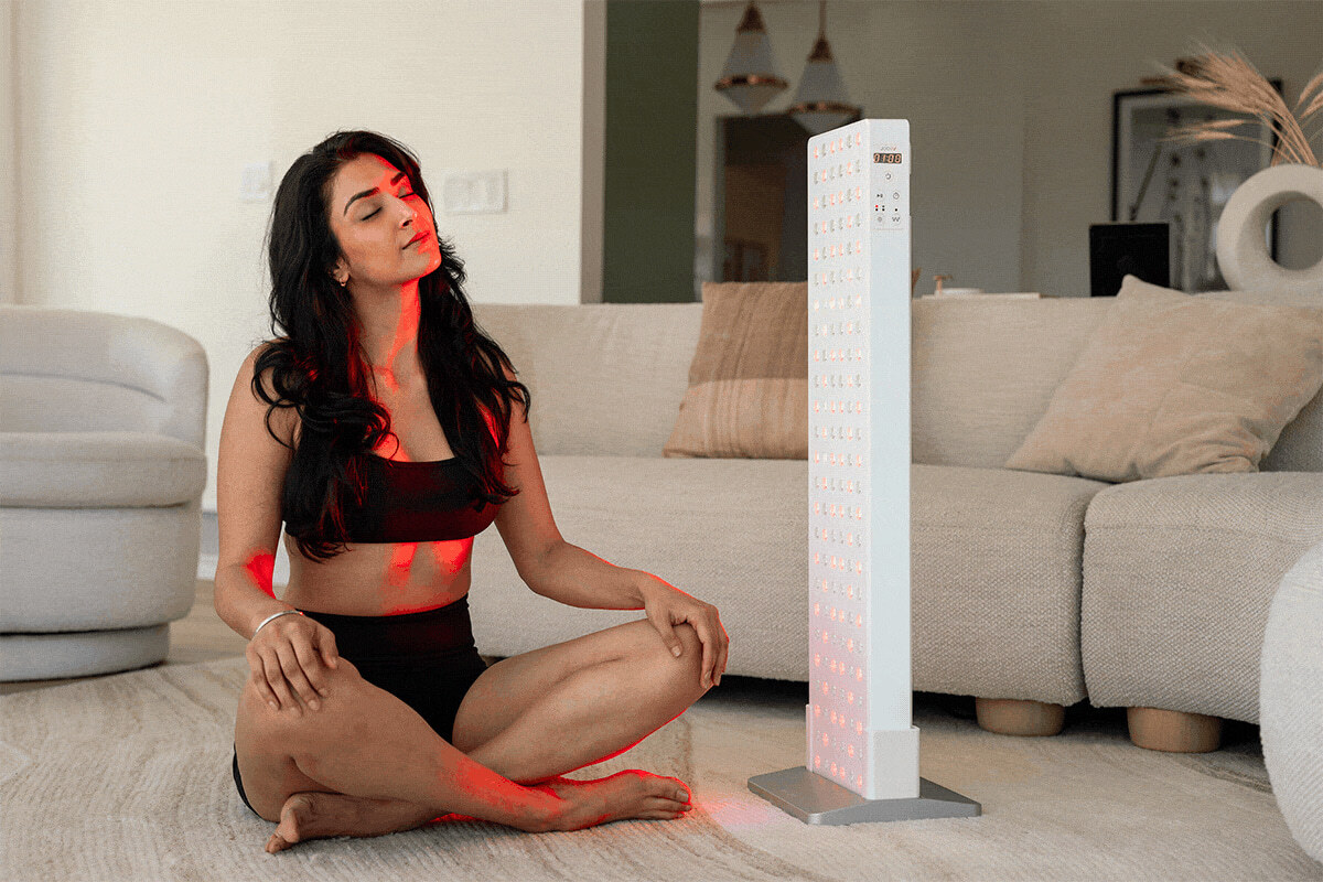 Woman sitting in front of a Joovv Solo device with boot floor stand on the ground.