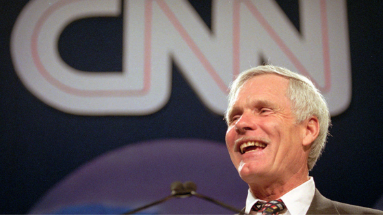 Ted Turner in front of the CNN logo.
