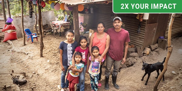 A family stands in front of their humble home made of scrap metal panels.