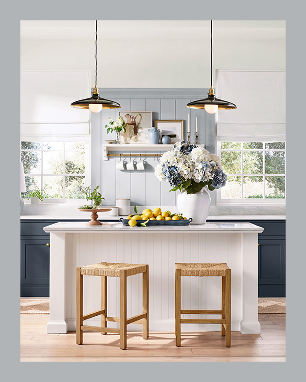 A luxurious open kitchen with navy cabinetry, a white shiplap kitchen island, rattan and wood barstools, and overhead pendant lighting.