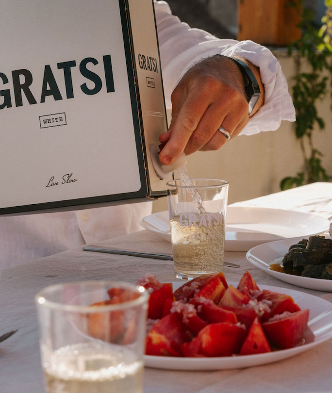 Man pouring a glass of Gratsi White Wine into a bàcarao glass at an outdoor dinner table.