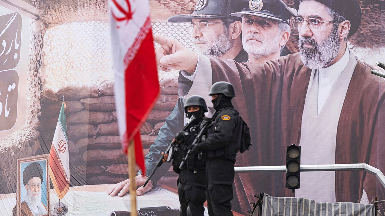 Two armed police officers stand  in front of a banner depicting Iran's new Supreme Leader, Ayatollah Mojtaba Khamenei, and military commanders on Quds Day, Tehran, Iran