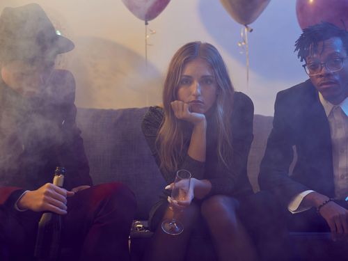Three people sitting on couch holding champagne and looking sad