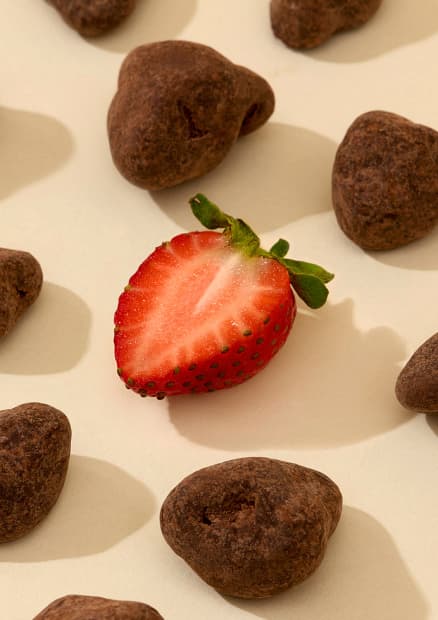 Chocolate-covered strawberries next to a fresh halved strawberry.