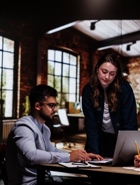 A senior student guides another student at a desk.