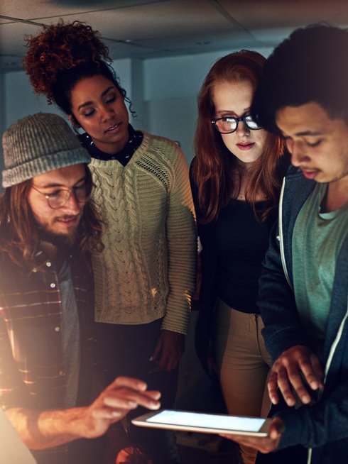 Four students standing around a tablet with intrigued expressions.