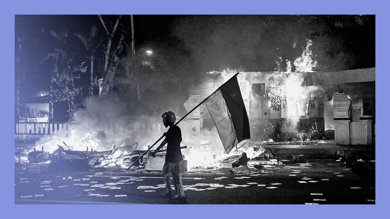 A protester walks with an Indonesian flag in front of a police headquarters that was set on fire and looted during demonstrations.