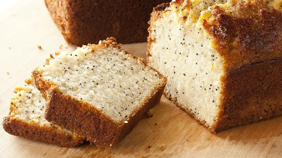 Close-up of a loaf of poppy seed tea bread, partially sliced.