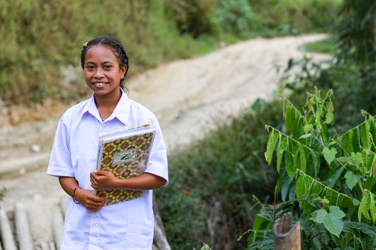 A teenage girl holds a book, preparing to walk a path to school.